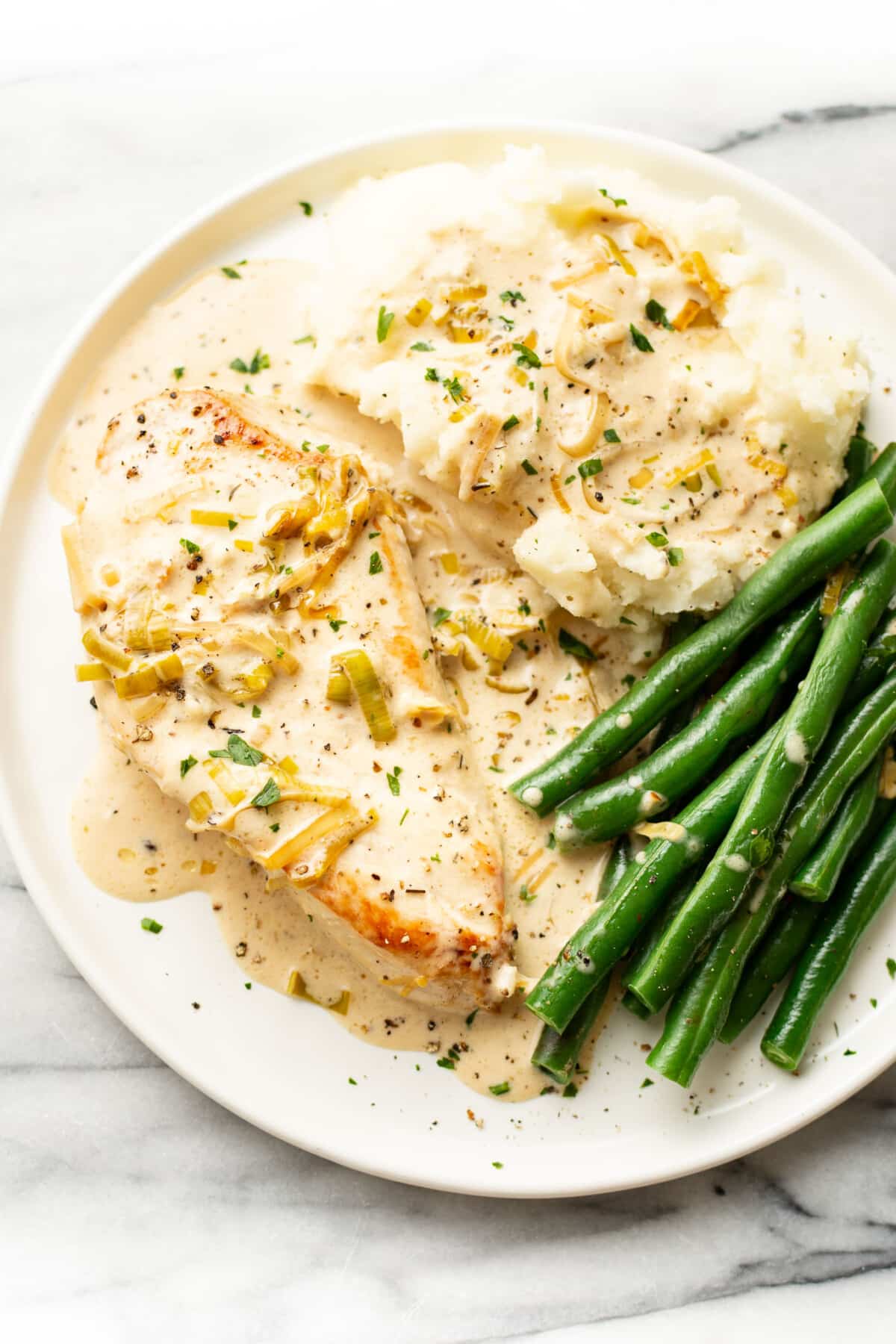 a plate with creamy leek chicken, mashed potatoes, and green beans