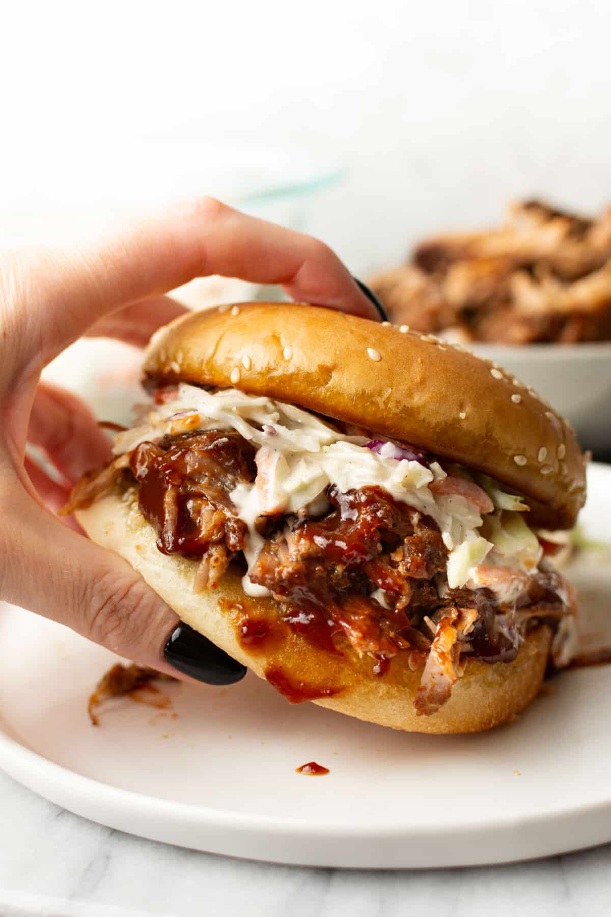a female hand holding a pulled pork sandwich