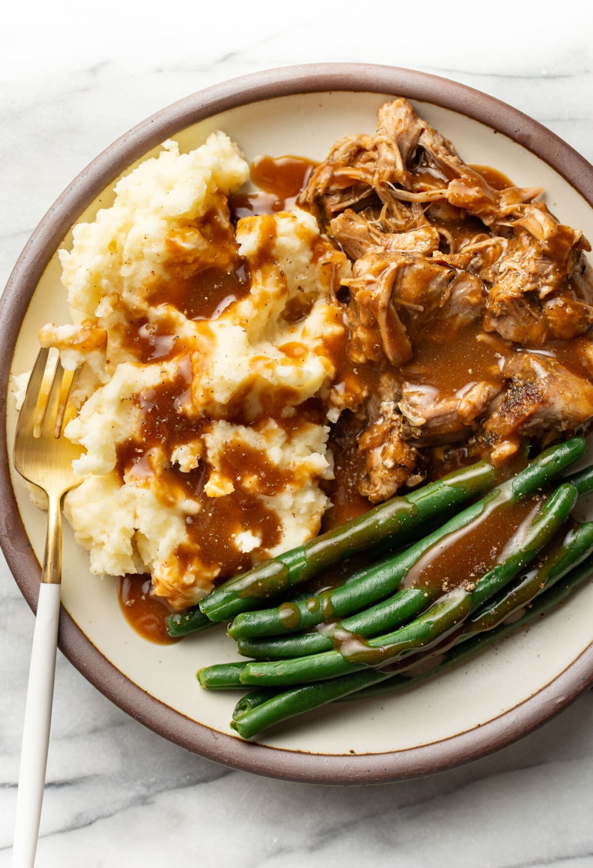 a plate with pork roast, green beans, mashed potatoes, gravy, and a fork