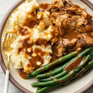 a plate with pork roast, green beans, mashed potatoes, gravy, and a fork