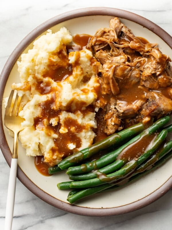 a plate with pork roast, green beans, mashed potatoes, gravy, and a fork