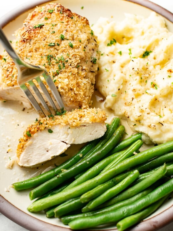 a plate with baked parmesan chicken, mashed potatoes, green beans, and a fork